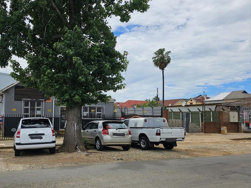 Exterior view of the office property featuring a grey facade, security gates, and an unpaved parking area with mature trees.