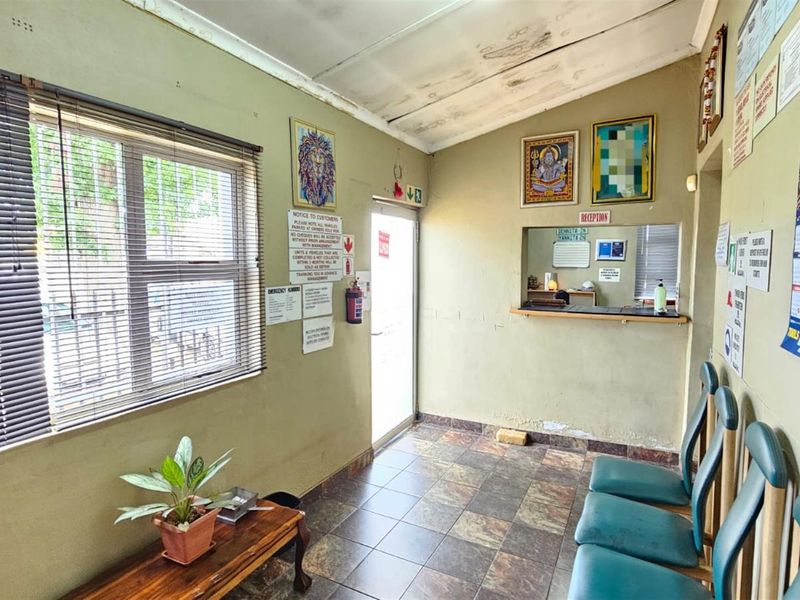 A functional office reception area featuring a service window, tiled flooring, and large windows with blinds, suitable for a professional workspace.