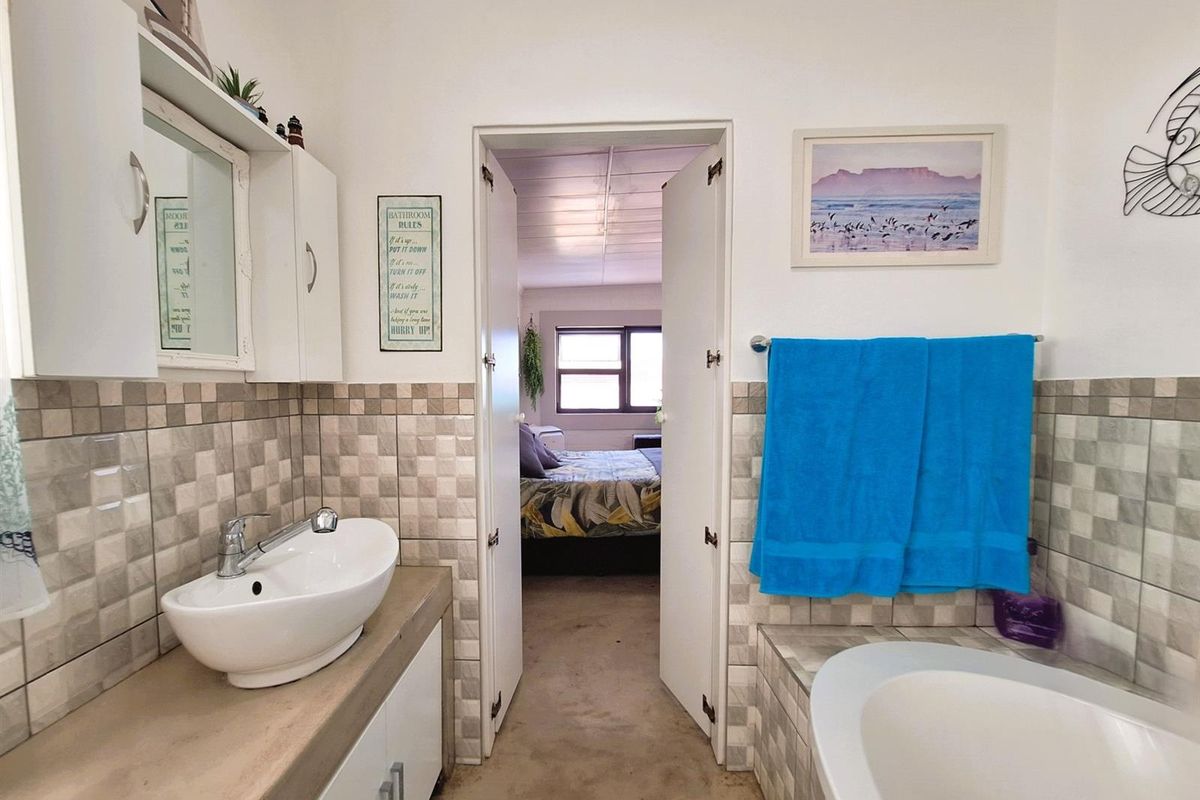 A functional bathroom featuring a vessel sink vanity, built-in bathtub, and tiled splashbacks, with direct access to an adjacent bedroom.