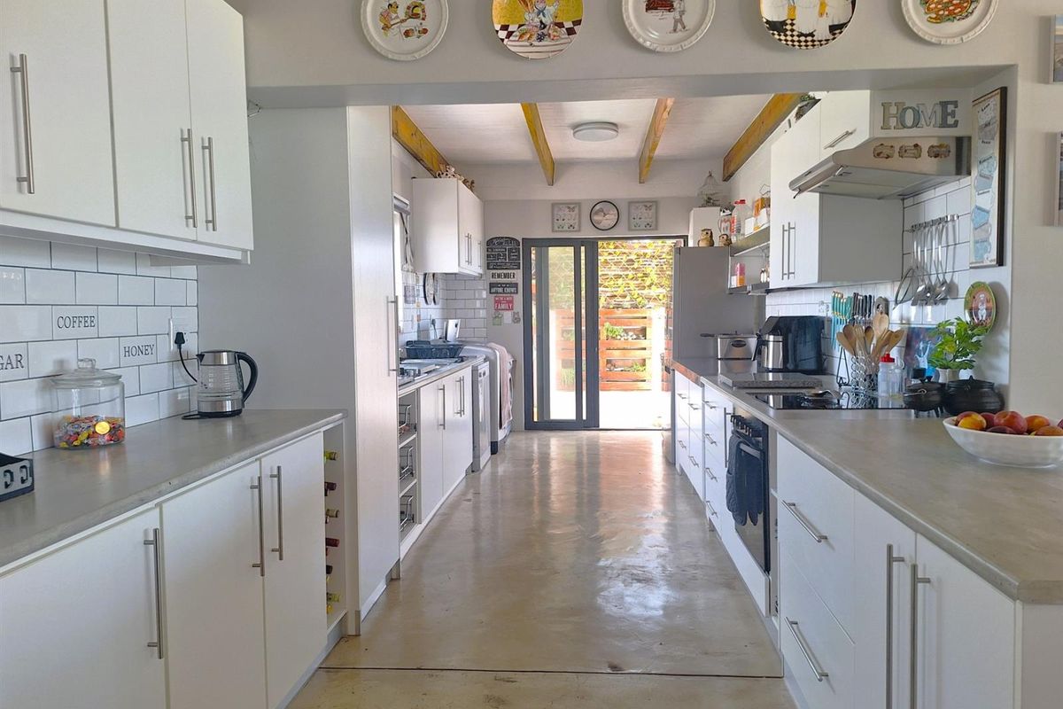 A functional galley-style kitchen featuring white cabinetry, subway tile backsplash, integrated oven and hob, and direct access to the rear outdoor area.