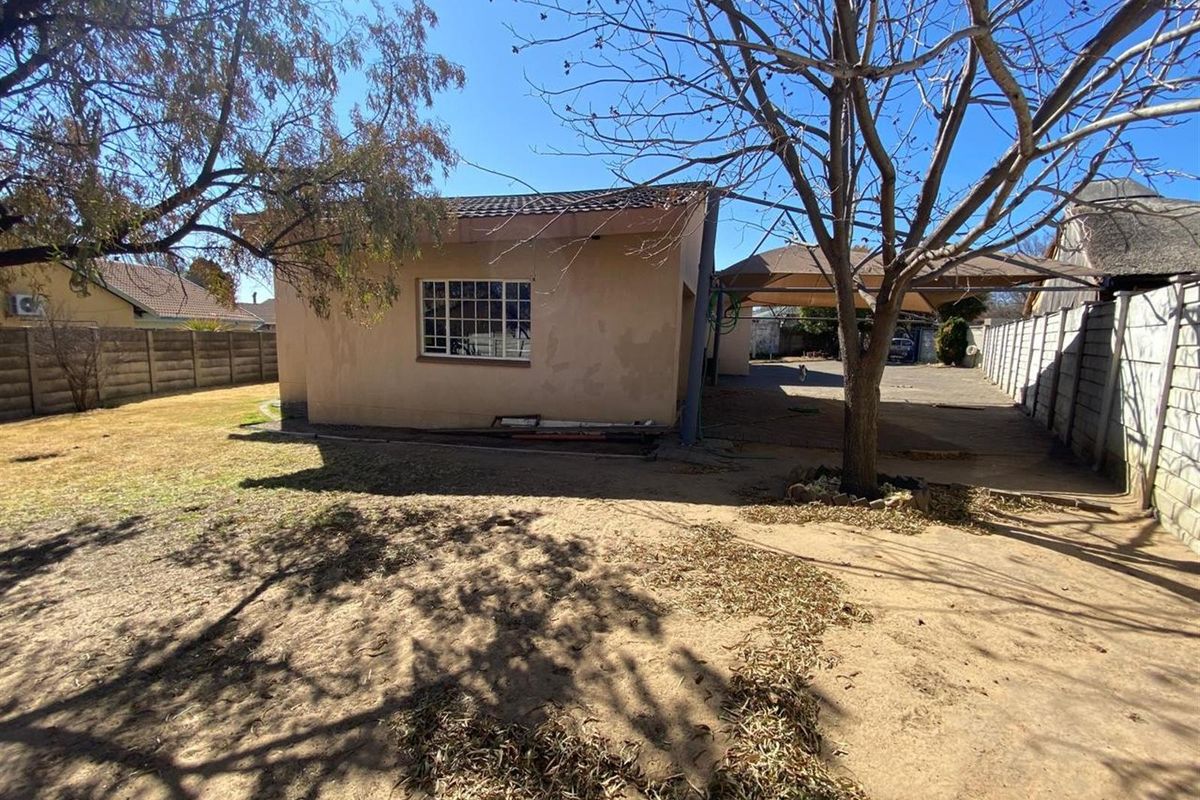 Rear view of the property featuring a concrete driveway, carport, and precast boundary walls, showing signs of exterior wear and maintenance requirements.