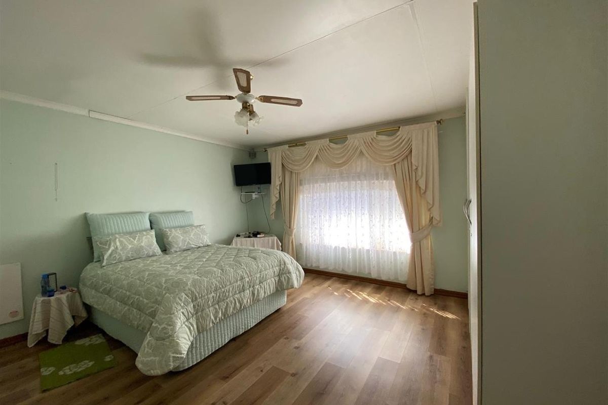 A spacious bedroom featuring laminate flooring, a ceiling fan, and built-in wardrobe storage.