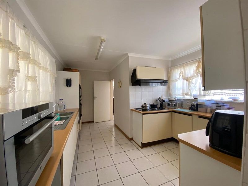 A functional kitchen featuring laminate countertops, built-in cabinetry, an electric hob with extractor fan, and tiled flooring.