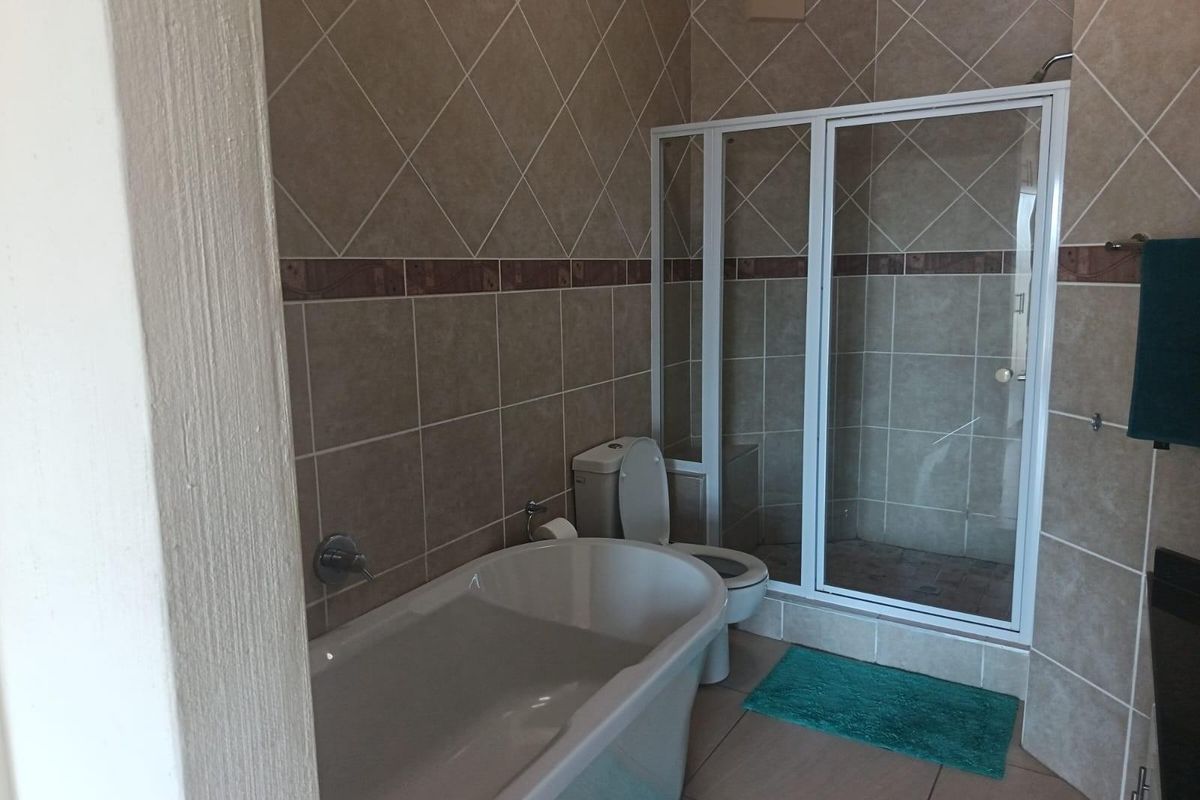 A functional bathroom featuring a freestanding bathtub, a separate shower enclosure with a white frame, and neutral wall tiling.