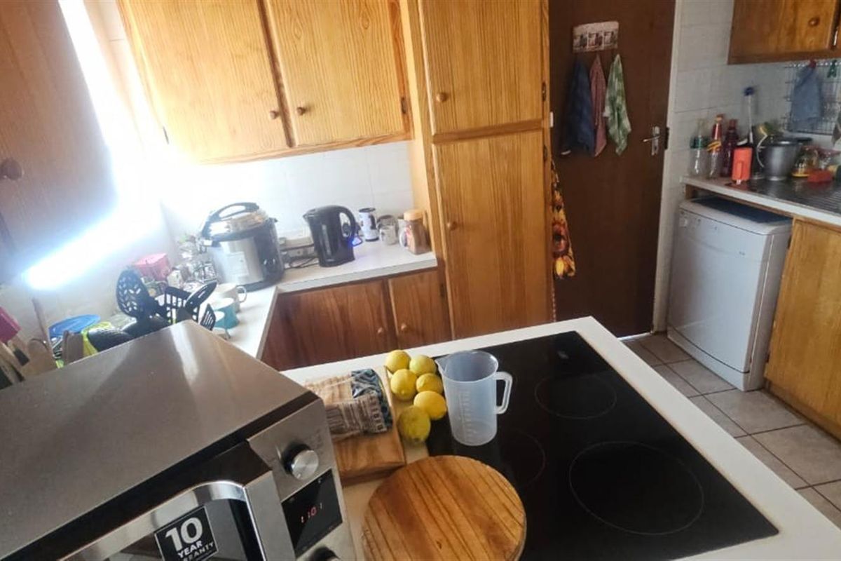 A functional kitchen featuring wooden cabinetry, a built-in electric hob, and tiled flooring, offering a practical layout for daily meal preparation.