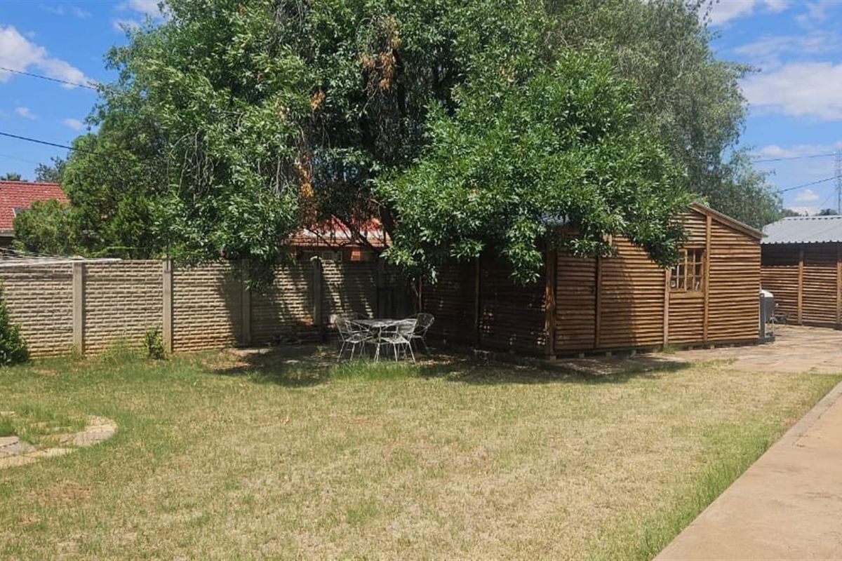 A spacious rear garden featuring a lawn, mature tree, paved walkway, and a wooden outbuilding structure.