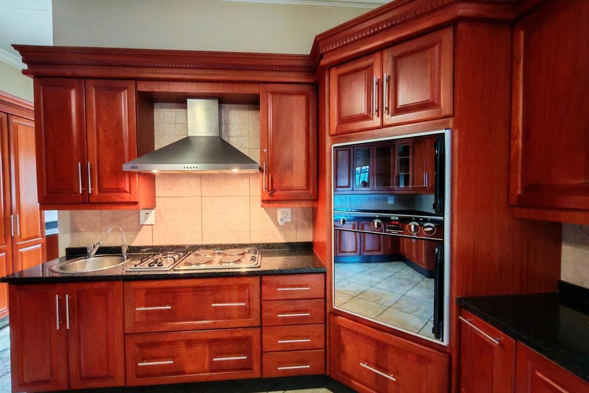 A traditional kitchen featuring rich wood cabinetry, granite countertops, a built-in oven, and a stainless steel extractor fan.