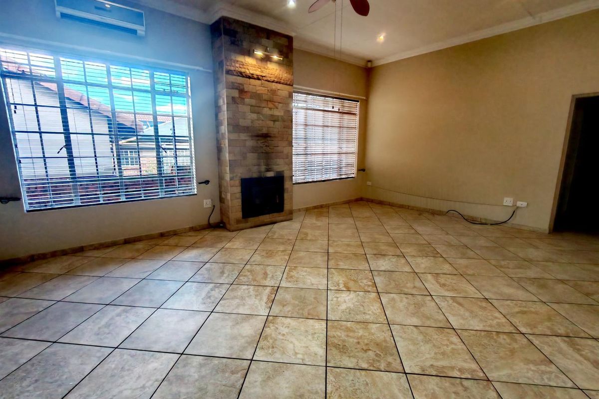 Spacious living room featuring tiled flooring, a prominent stone-clad fireplace, ceiling fan, and wall-mounted air conditioning unit.
