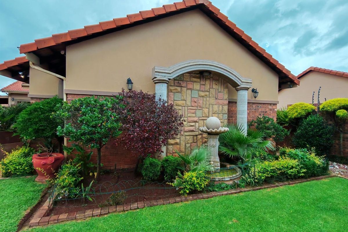A well-maintained rear garden area featuring a decorative stone-clad feature wall with columns, a stone water fountain, and established landscaping.