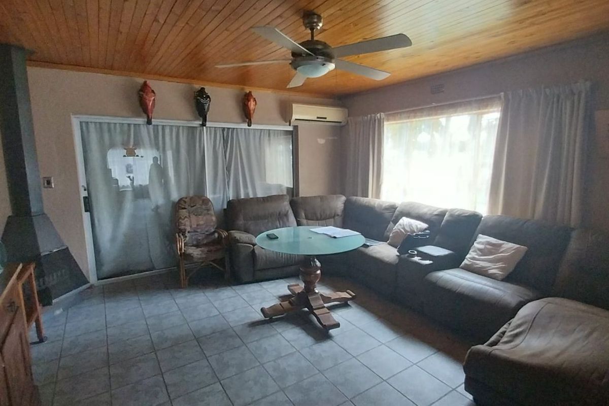 A living room featuring a timber-clad ceiling, tiled flooring, a built-in fireplace, and a ceiling fan, providing a functional and cozy living space.