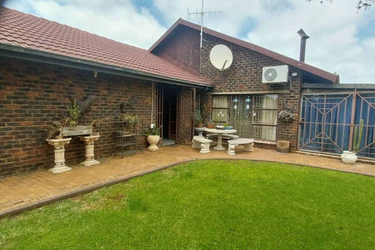 Rear view of a brick house featuring a paved patio area, well-maintained lawn, and exterior wall-mounted air conditioning unit.