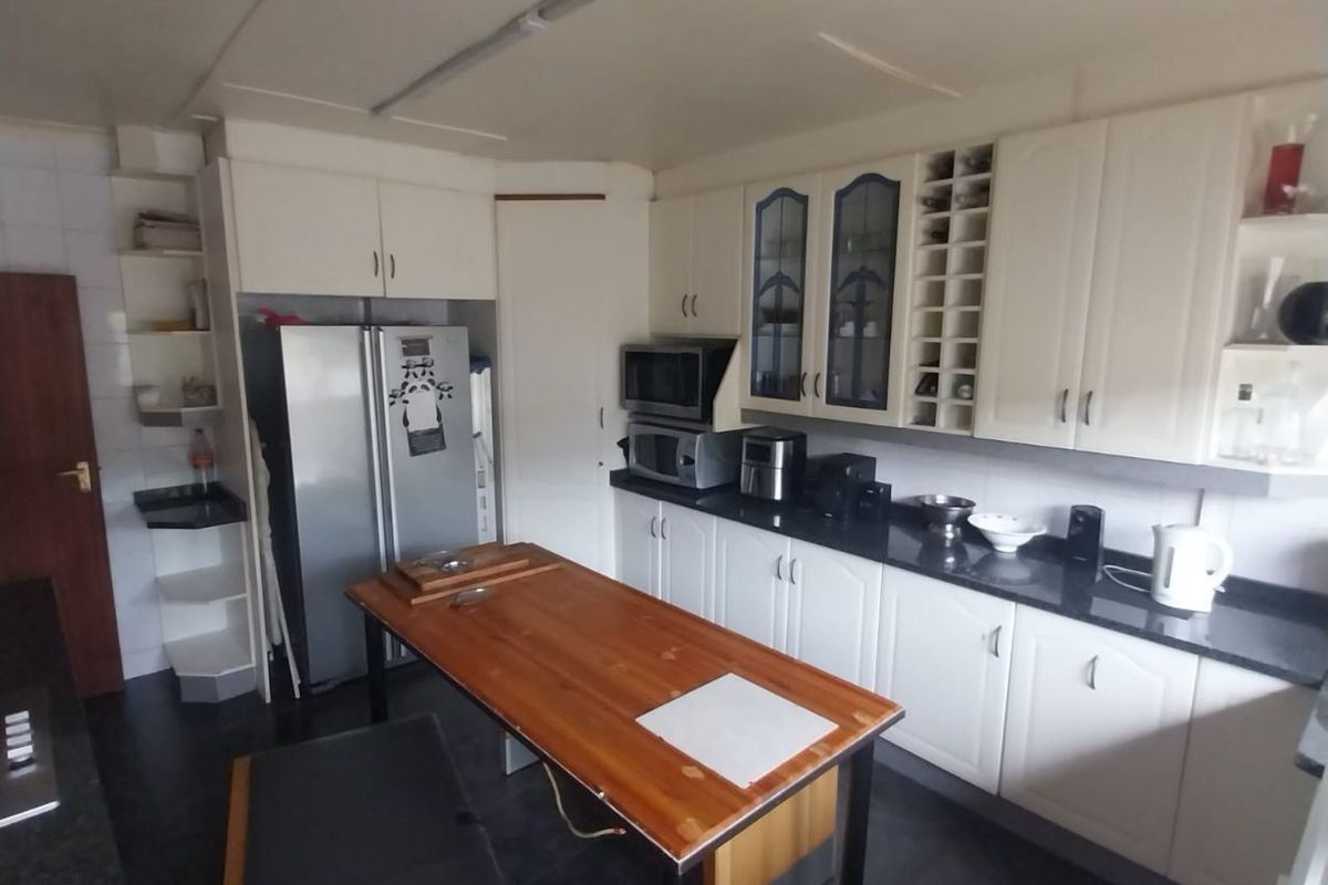 A functional kitchen featuring white cabinetry, dark granite countertops, built-in microwave, and a central wooden island with integrated seating.