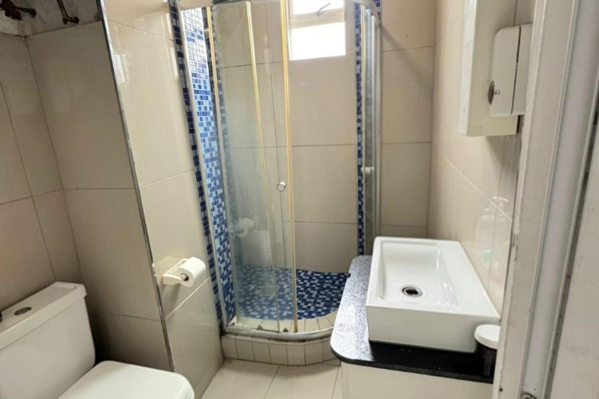 Compact bathroom featuring a corner shower enclosure, vanity basin, and toilet with tiled finishes and exposed water heater unit.