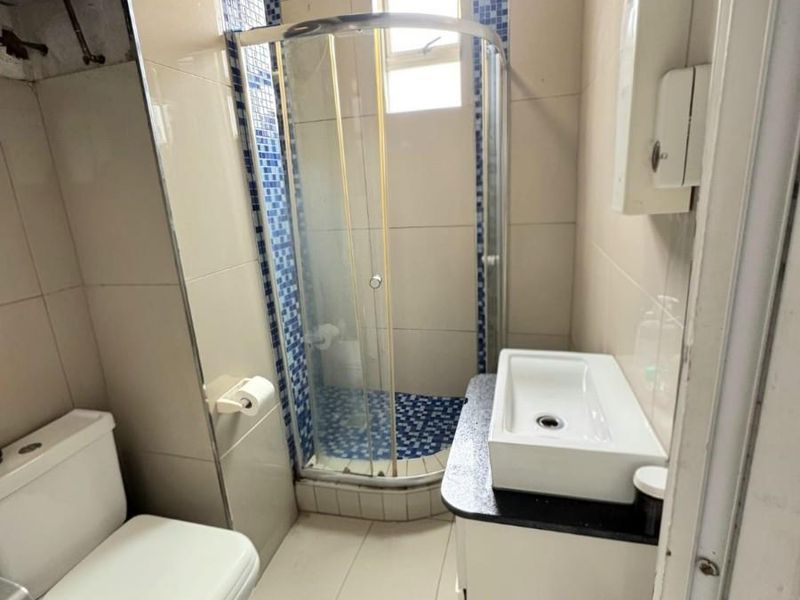 Compact bathroom featuring a corner shower enclosure, vanity basin, and toilet with tiled finishes and exposed water heater unit.