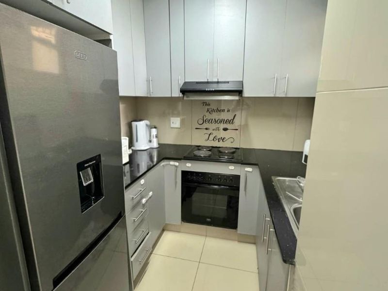 Compact kitchen featuring modern grey cabinetry, black granite countertops, built-in oven, electric hob, and tiled flooring.