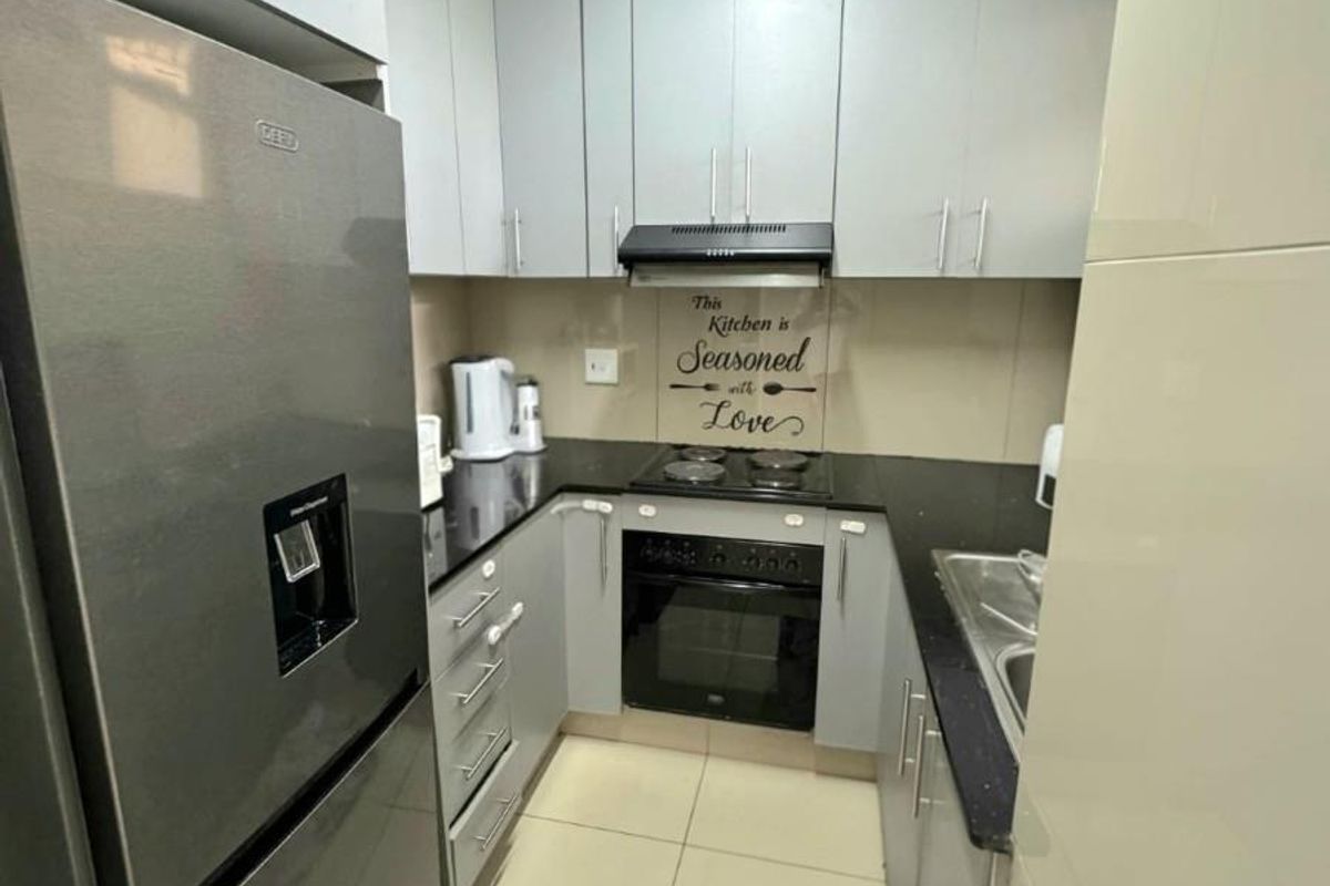Compact kitchen featuring modern grey cabinetry, black granite countertops, built-in oven, electric hob, and tiled flooring.