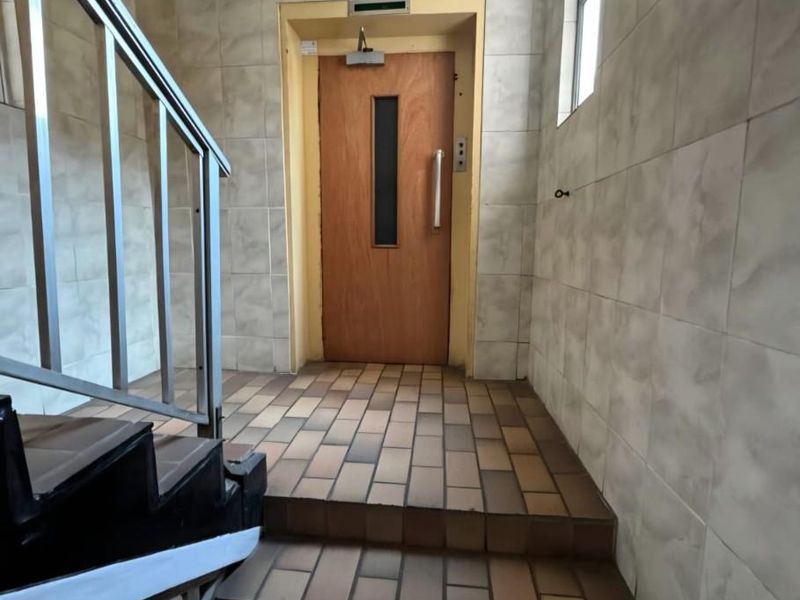 A functional apartment building hallway featuring tiled flooring, tiled walls, and a metal handrail leading to an elevator entrance.