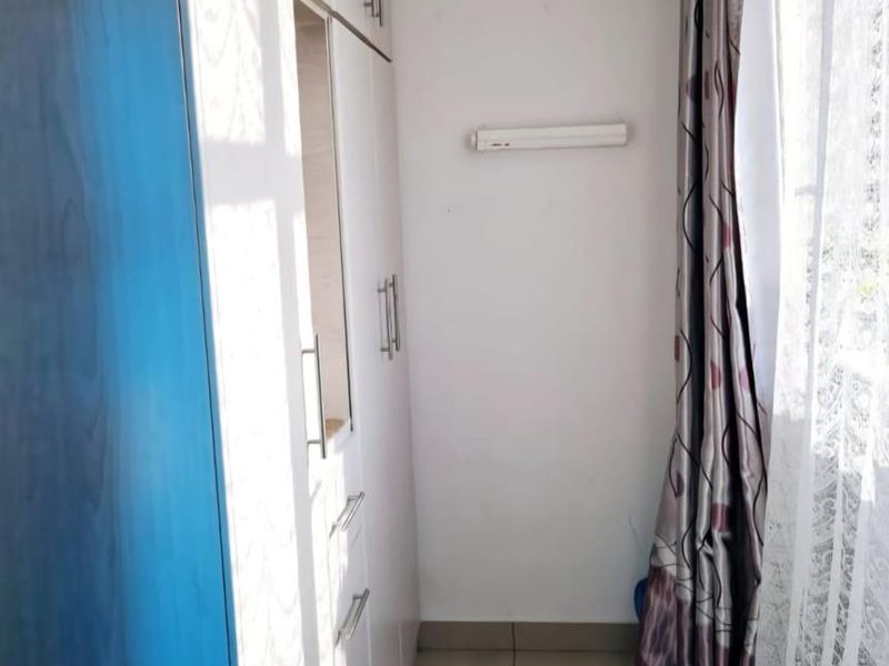 A compact bedroom area featuring built-in cupboards with blue and white cabinetry and neutral tiled flooring.