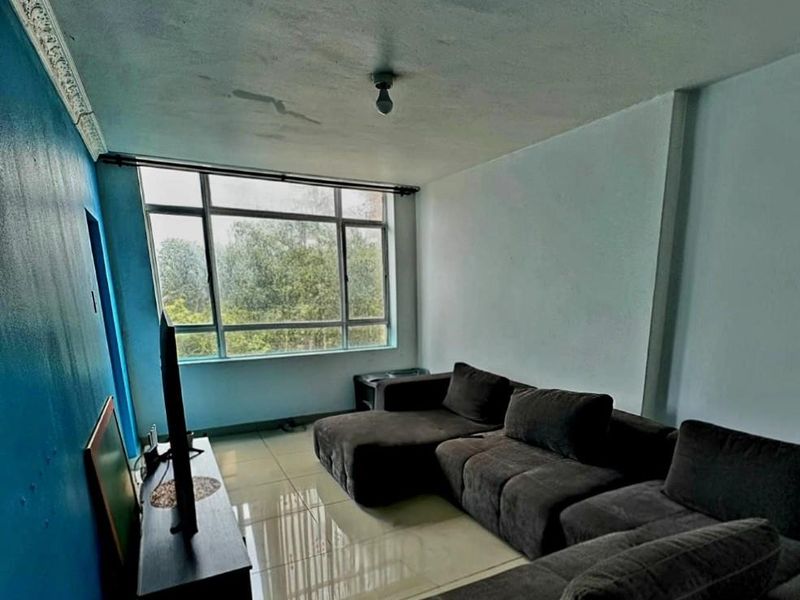 A living room featuring large windows, tiled flooring, and decorative ceiling cornicing, currently showing signs of ceiling water damage and uneven wall finishes.
