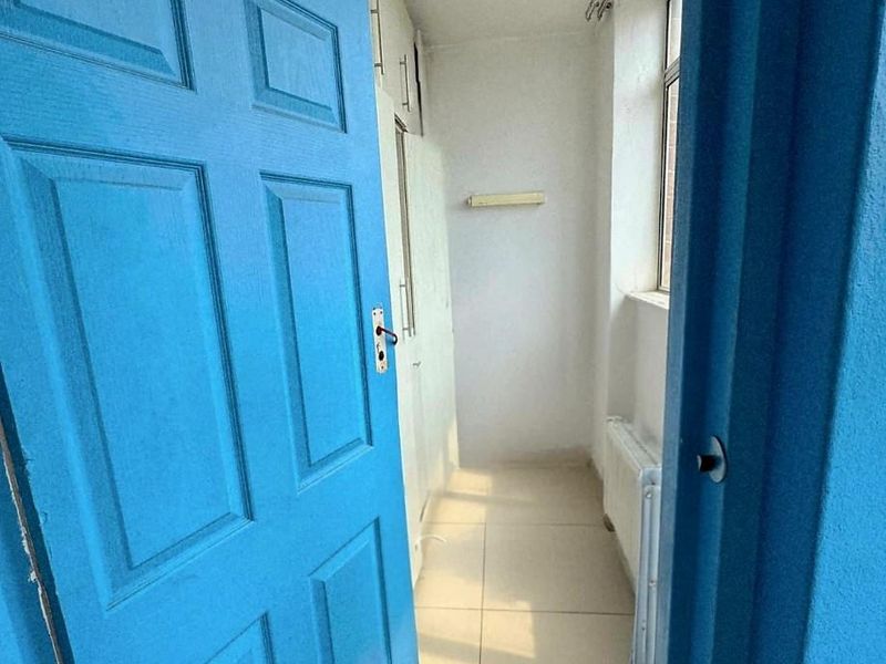 A narrow hallway featuring tiled flooring, built-in storage cabinetry, and a wall-mounted radiator.