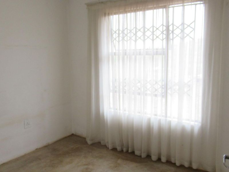 An empty bedroom featuring a window with a security gate and plain wall finishes, ready for renovation or staging.
