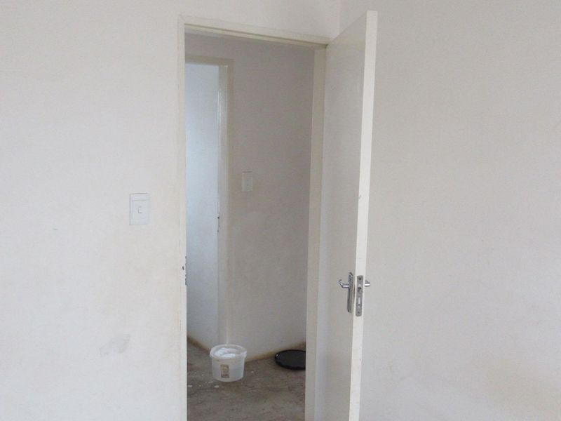 A view through an open doorway into an empty, unfinished interior space with plain white walls and exposed flooring.