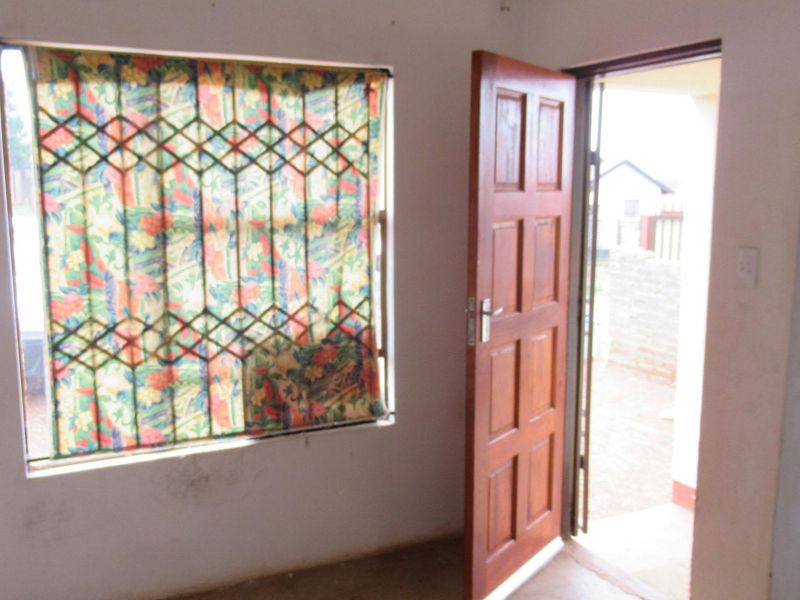 An empty entry area featuring a timber panel door and a window fitted with security bars, showing signs of wear.