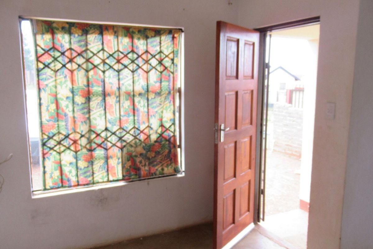 An empty entry area featuring a timber panel door and a window fitted with security bars, showing signs of wear.