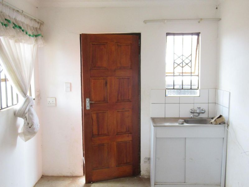 A functional scullery or utility area featuring a stainless steel sink, tiled splashback, and direct exterior access via a timber door.