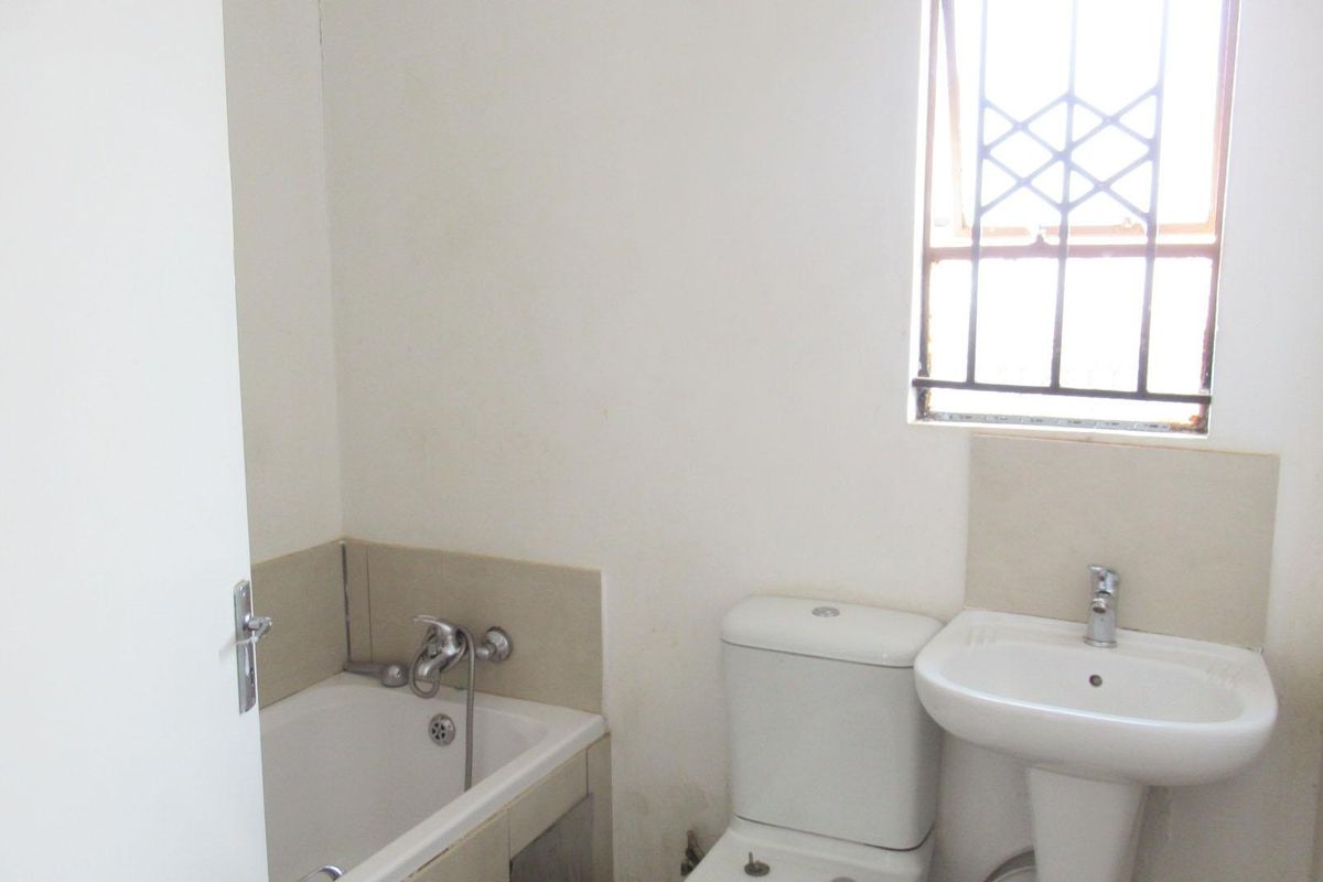 A compact bathroom featuring a bathtub, pedestal basin, and toilet, with a window fitted with security burglar bars.