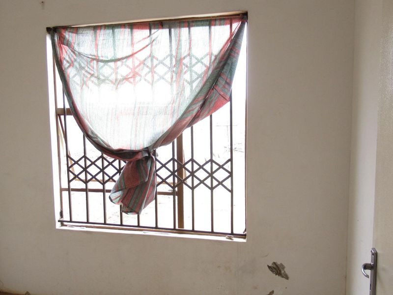 An empty bedroom featuring a window with a fitted security gate and visible wall plaster damage.