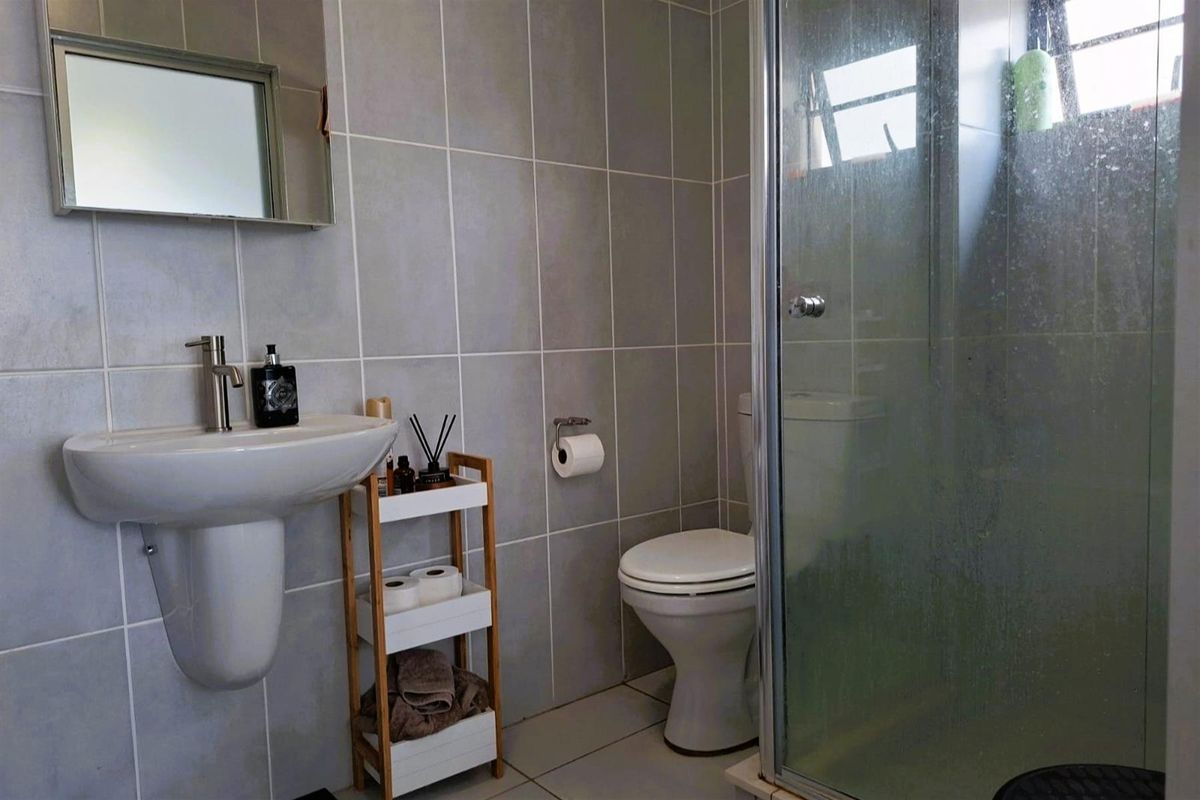 A functional bathroom featuring a pedestal basin, toilet, and a glass-enclosed shower with neutral wall tiling.
