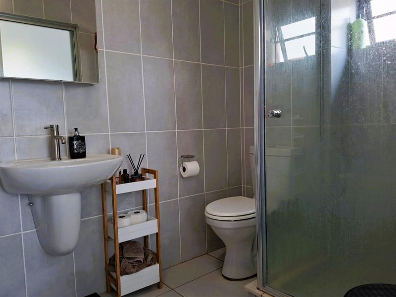 A functional bathroom featuring a pedestal basin, toilet, and a glass-enclosed shower with neutral wall tiling.
