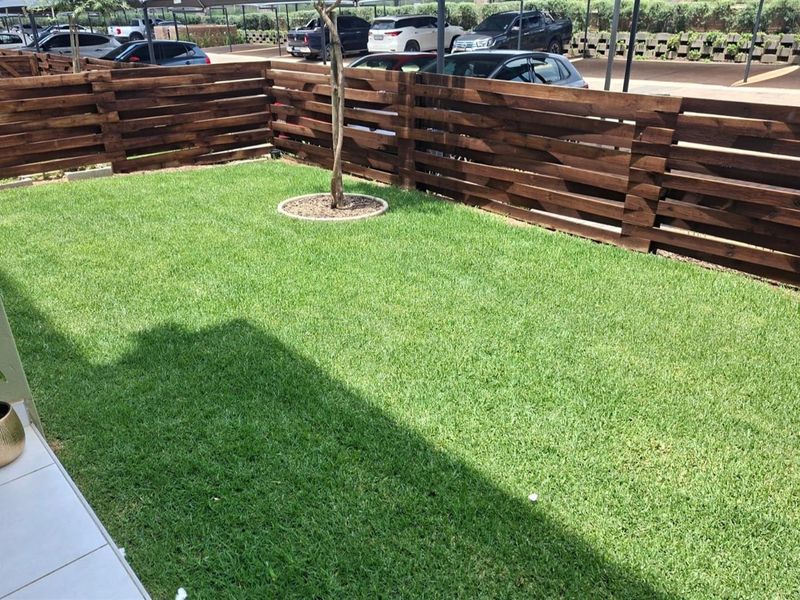 A well-maintained private garden area featuring a neat lawn, established tree, and timber slat boundary fencing.