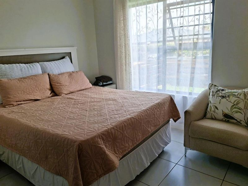 A comfortable bedroom featuring tiled flooring and a large window fitted with security bars, allowing for natural light.