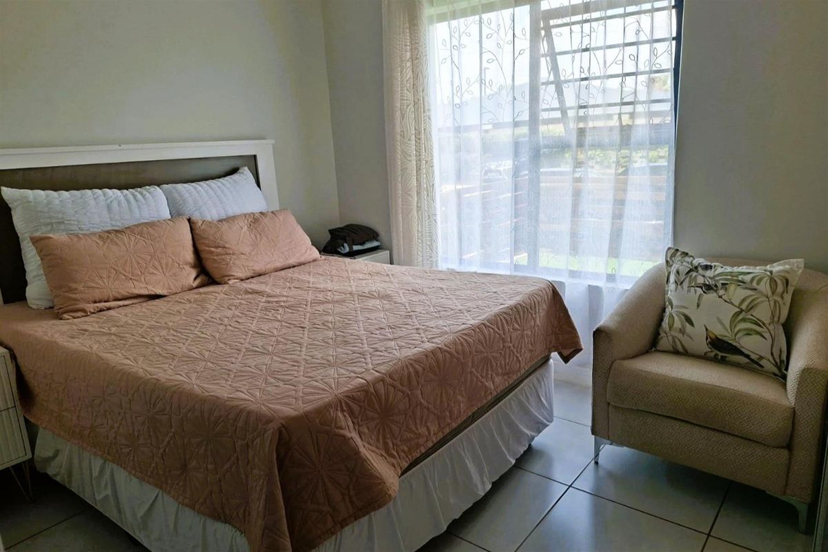 A comfortable bedroom featuring tiled flooring and a large window fitted with security bars, allowing for natural light.