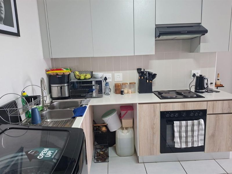 A functional kitchen featuring modern light-toned cabinetry, a built-in oven with electric hob, extractor fan, and a stainless steel sink with tiled backsplash.