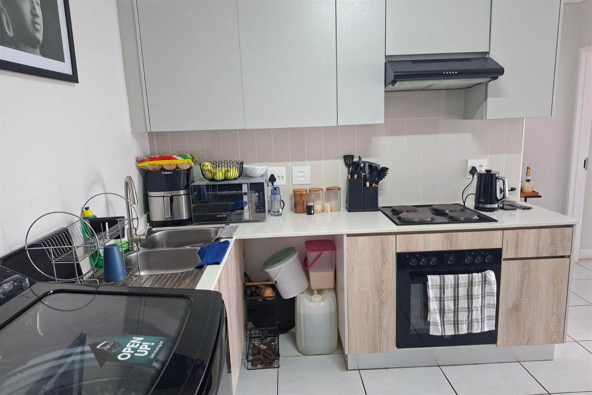 A functional kitchen featuring modern light-toned cabinetry, a built-in oven with electric hob, extractor fan, and a stainless steel sink with tiled backsplash.
