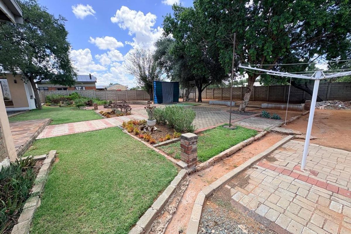 Spacious rear garden featuring paved walkways, established trees, lawn areas, and perimeter walling, providing a functional outdoor space.