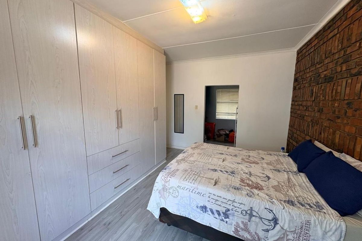 A bedroom featuring light wood-grain built-in cupboards, laminate flooring, and a rustic exposed brick feature wall.