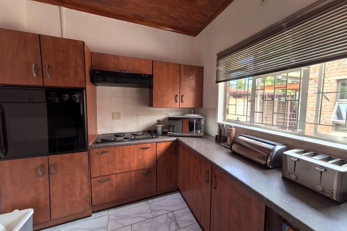 Functional kitchen featuring wood-toned cabinetry, built-in oven, electric hob, extractor fan, and tiled flooring with a window overlooking the exterior.