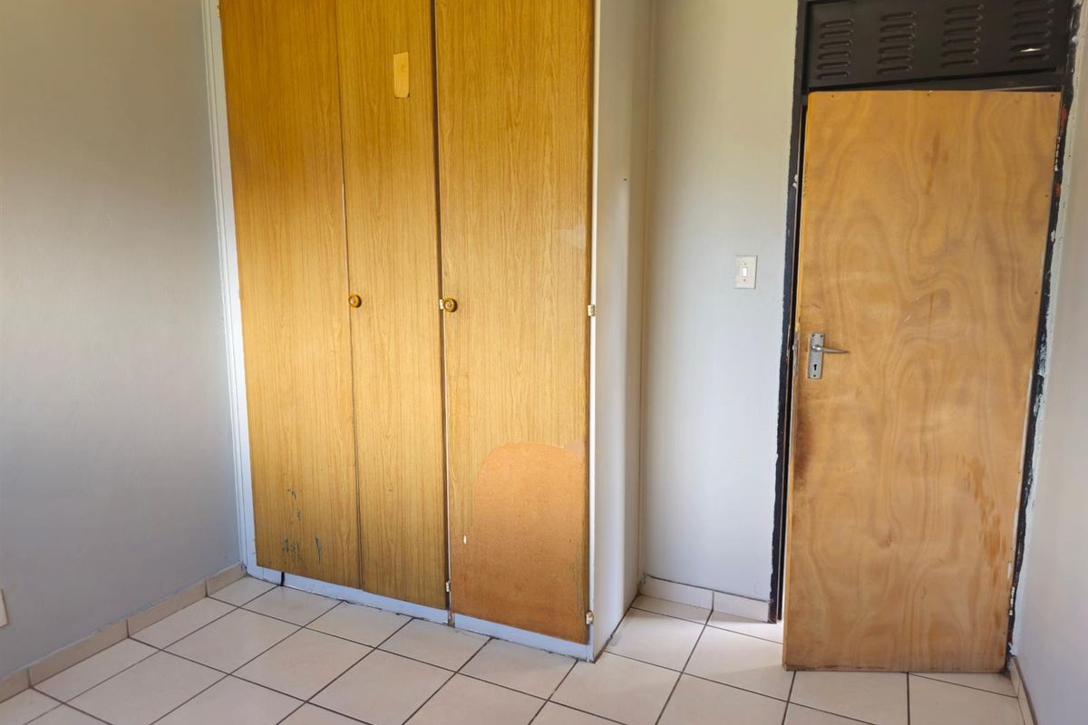 A bedroom featuring built-in wooden wardrobes, tiled flooring, and a wooden door with a ventilation panel.