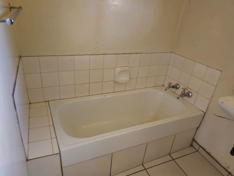A dated bathroom featuring a built-in bathtub with tiled surround, chrome fixtures, and a wall-mounted soap dish.