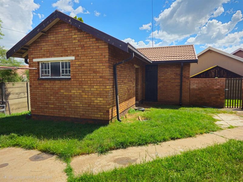 A view of the rear exterior of a brick house featuring a tiled roof, guttering system, and a concrete pathway leading to the entrance.
