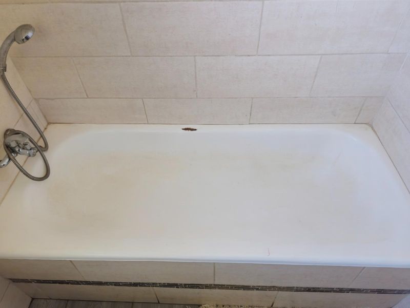 A standard bathtub featuring a handheld shower attachment and tiled surround, showing visible wear and enamel damage.