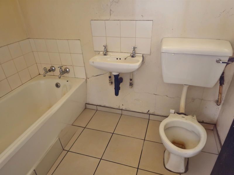 A dated bathroom featuring a standard bathtub, wall-mounted basin, and toilet, requiring significant renovation and repair to wall finishes and fixtures.