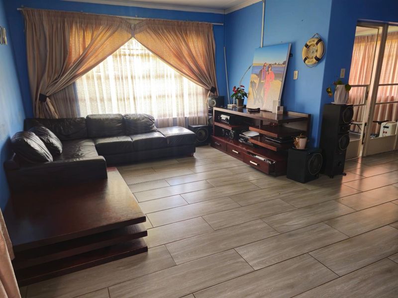 A living room featuring wood-look tile flooring and a large window with curtains, providing a functional space for relaxation.