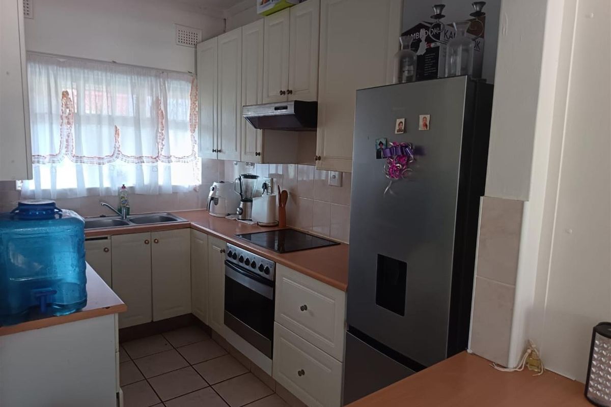 A functional kitchen featuring built-in cabinetry, laminate countertops, a stainless steel double sink, and integrated cooking appliances with tiled flooring and backsplash.