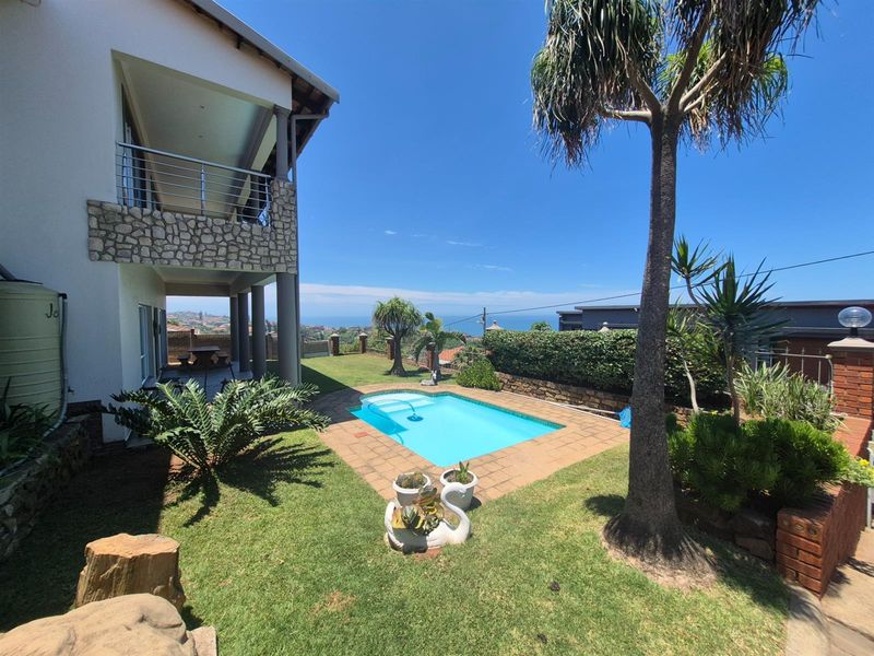 A rear exterior view featuring a swimming pool, landscaped garden, and a covered patio area with stone cladding and stainless steel balustrades.