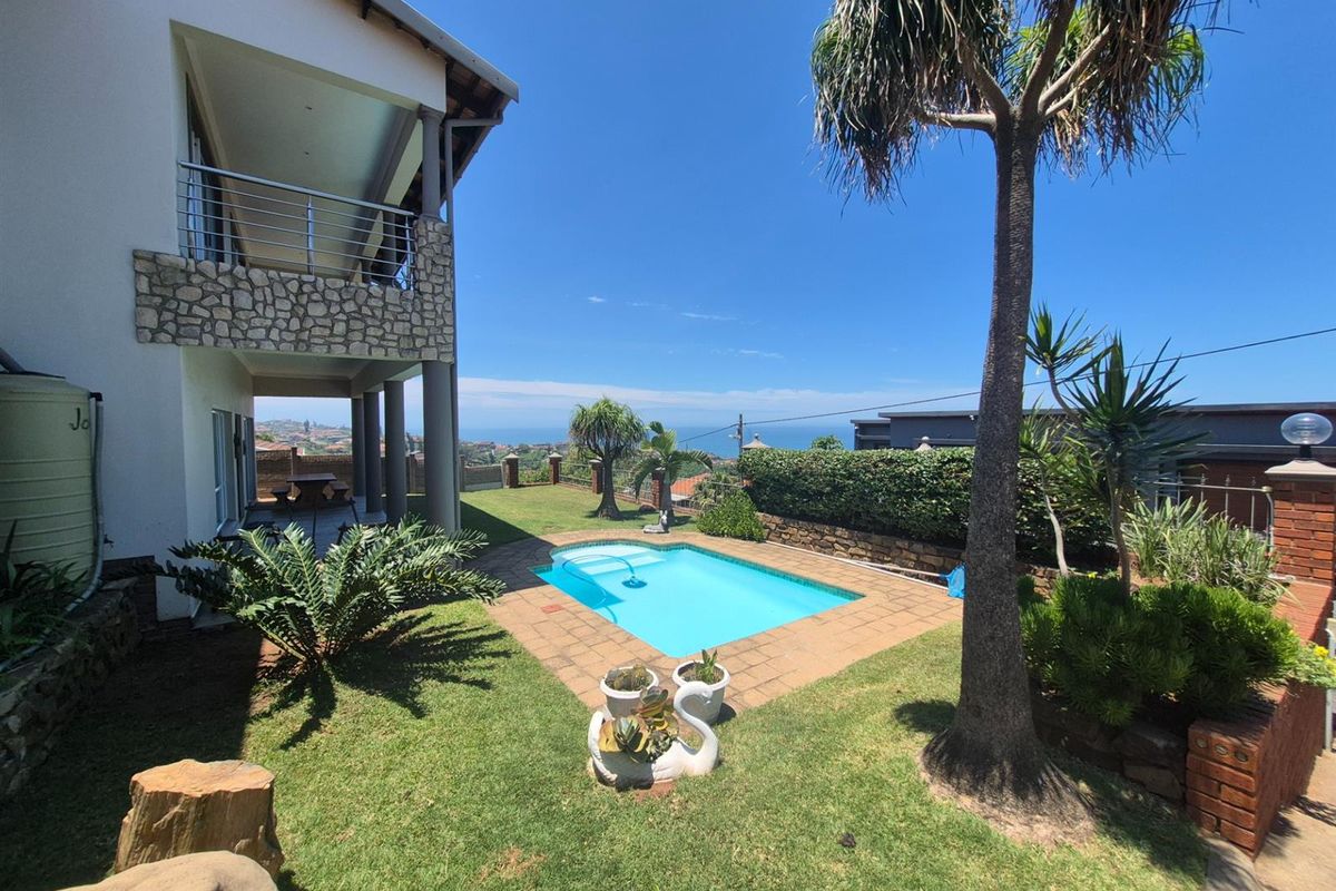 A rear exterior view featuring a swimming pool, landscaped garden, and a covered patio area with stone cladding and stainless steel balustrades.